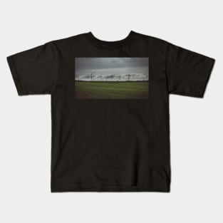 Moody sky over meadow and power lines Kids T-Shirt